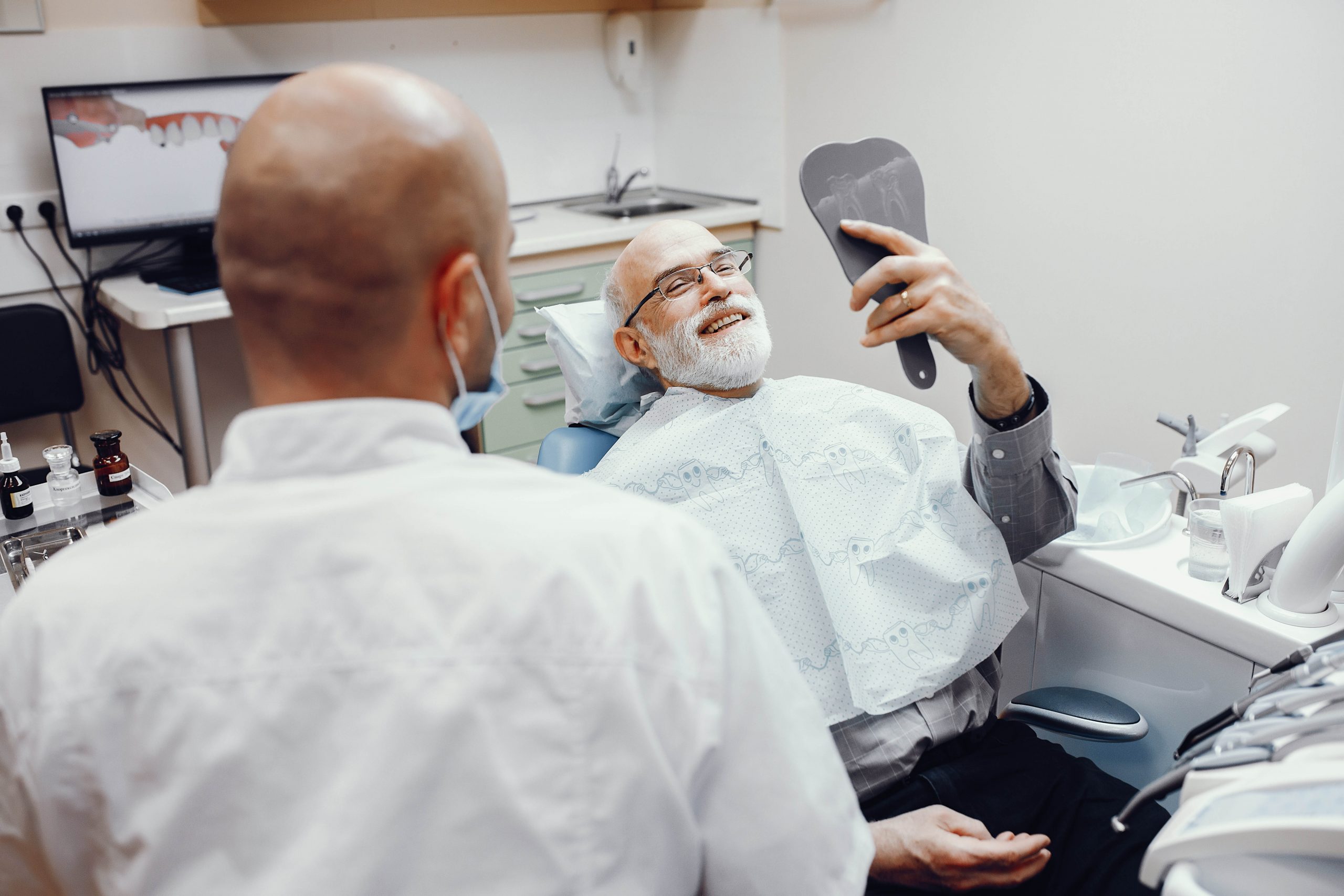 Handsome old man talking to the dendist. Two men in the dentist's office. Grandfather looking into the mirror on his teeth