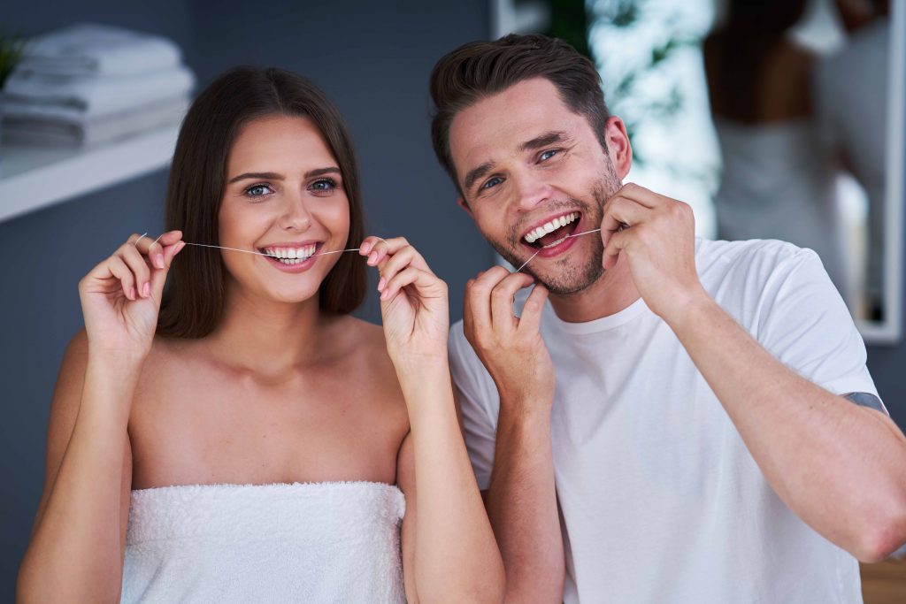 Happy young couple flossing teeth in the bathroom