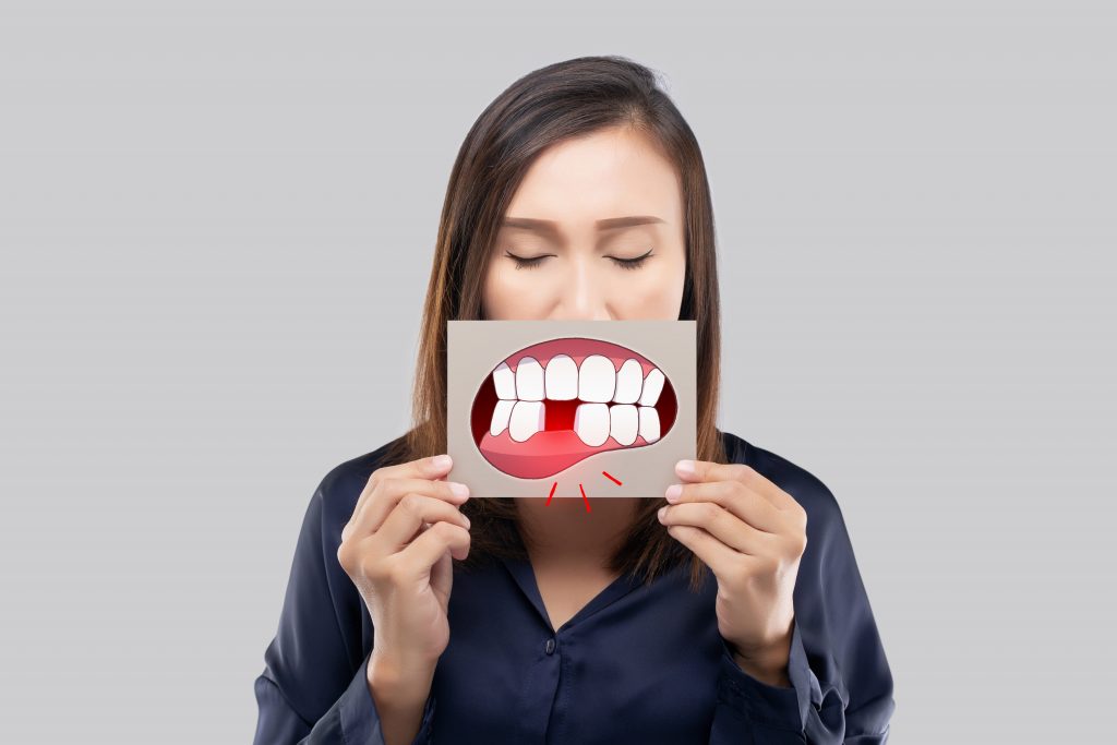 Asian woman in the dark blue shirt holding a brown paper with the broken tooth cartoon picture of his mouth against the gray background, Decayed tooth, The concept with healthcare gums and teeth