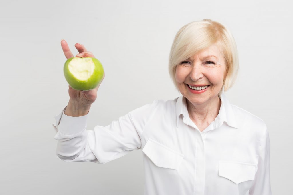 A beautiful mature woman holding a bitten green apple in right hand. She wants to show that she has a good and stron teeth. Isolated on white background