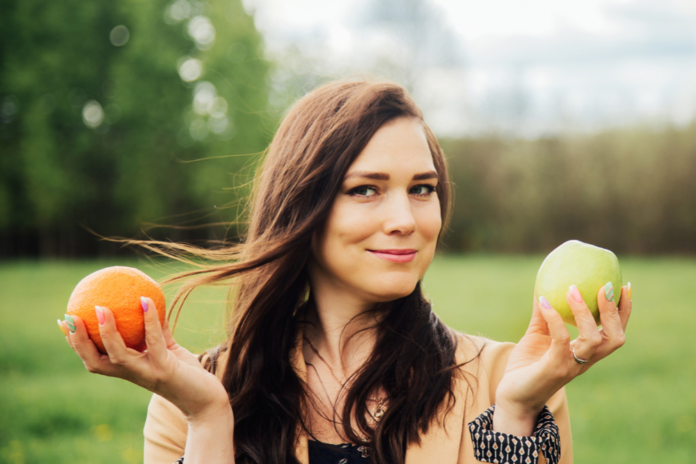 Femme souriante dehors tenant une orange et une pomme