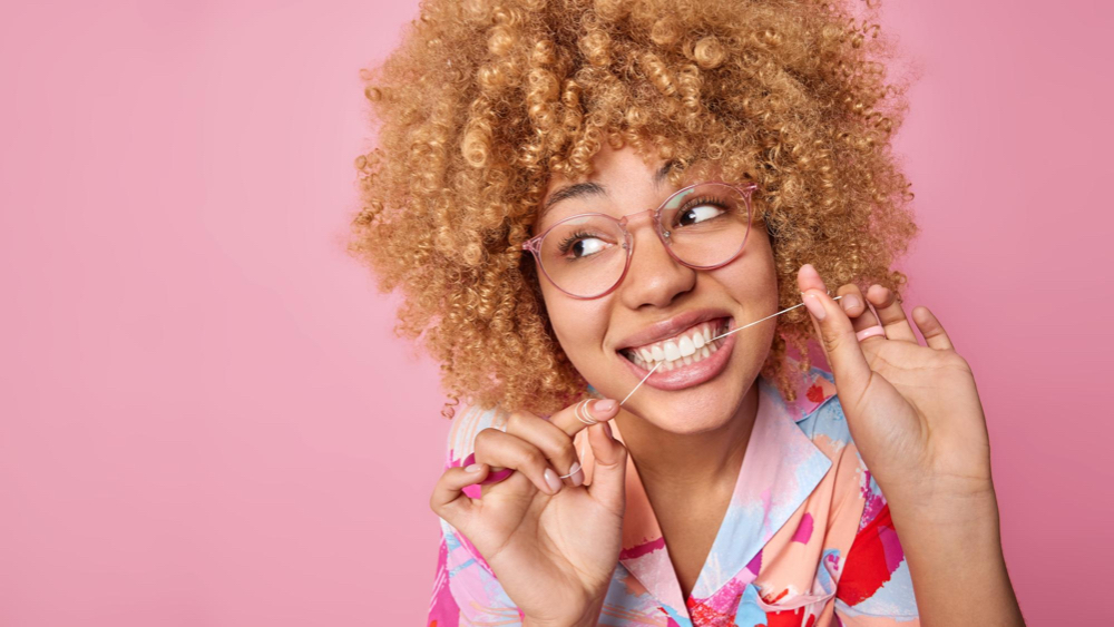 femme souriante passe la soie dentaire fond rose