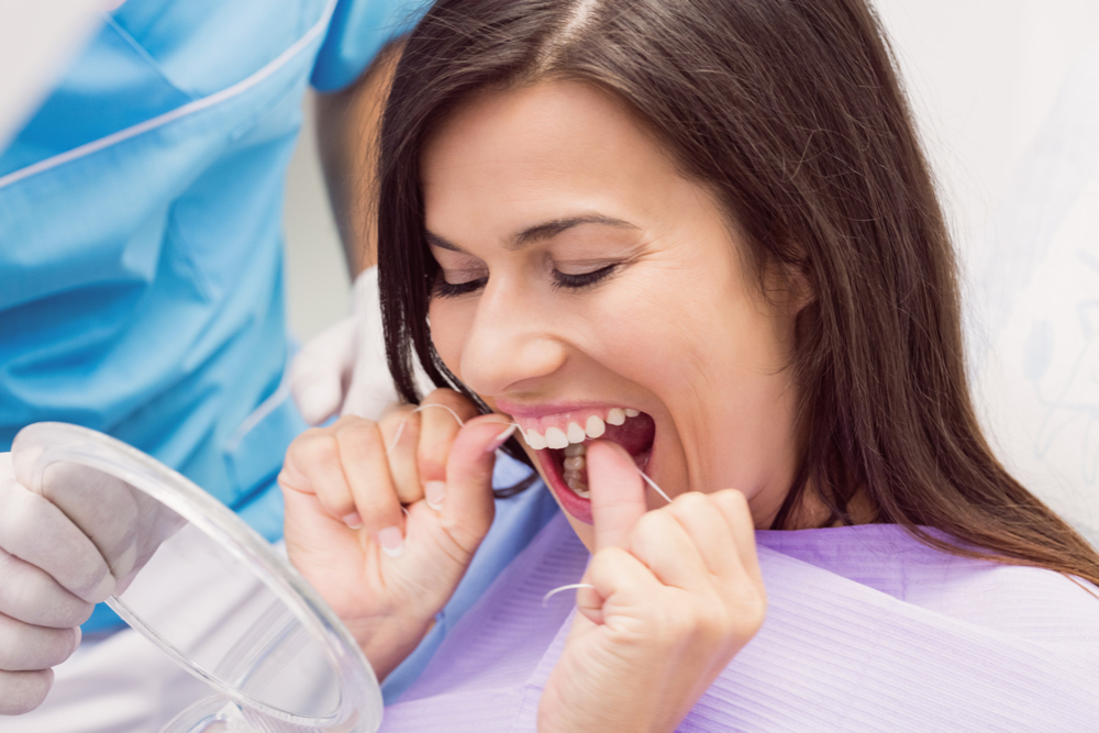 woman using dental floss in front of mirror