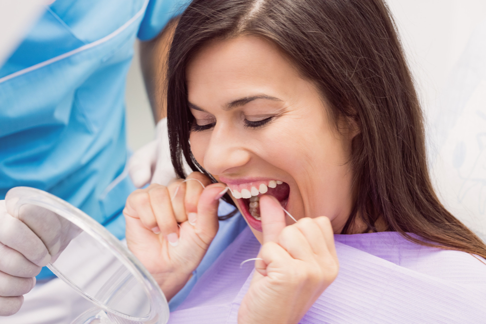 femme passe la soie dentaire entre ses dents devant un miroir