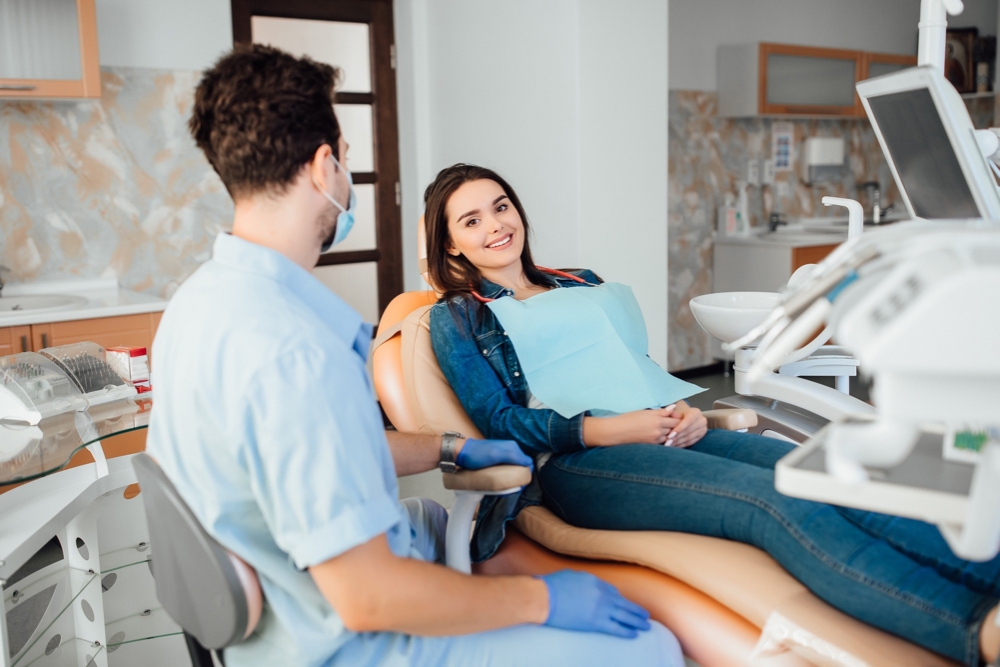 femme assise sur siège chez le dentiste souriante avec homme masque de dos à boucherville