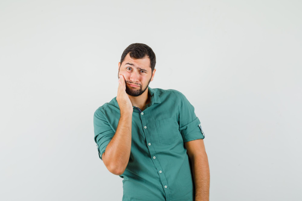 man holding his painful jaw because of untreated wisdom teeth on grey background