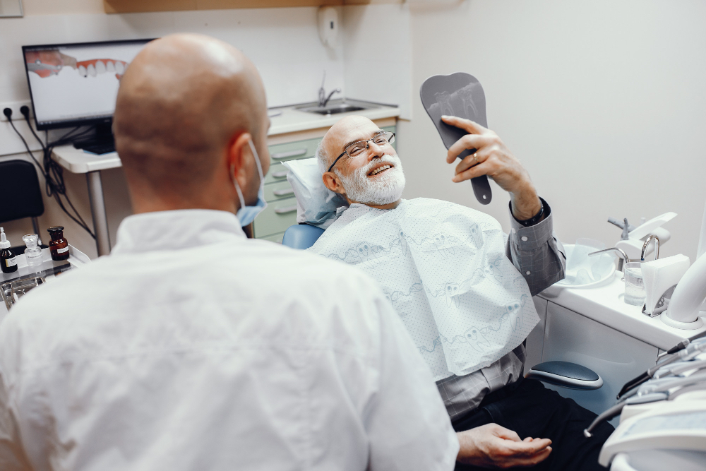 senior at the dentist holding mirror smiling at his reflection with healthy teeth